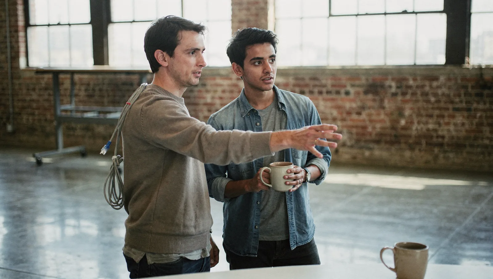 Two software engineers standing in an industrial office discussing plans near an exposed brick wall.